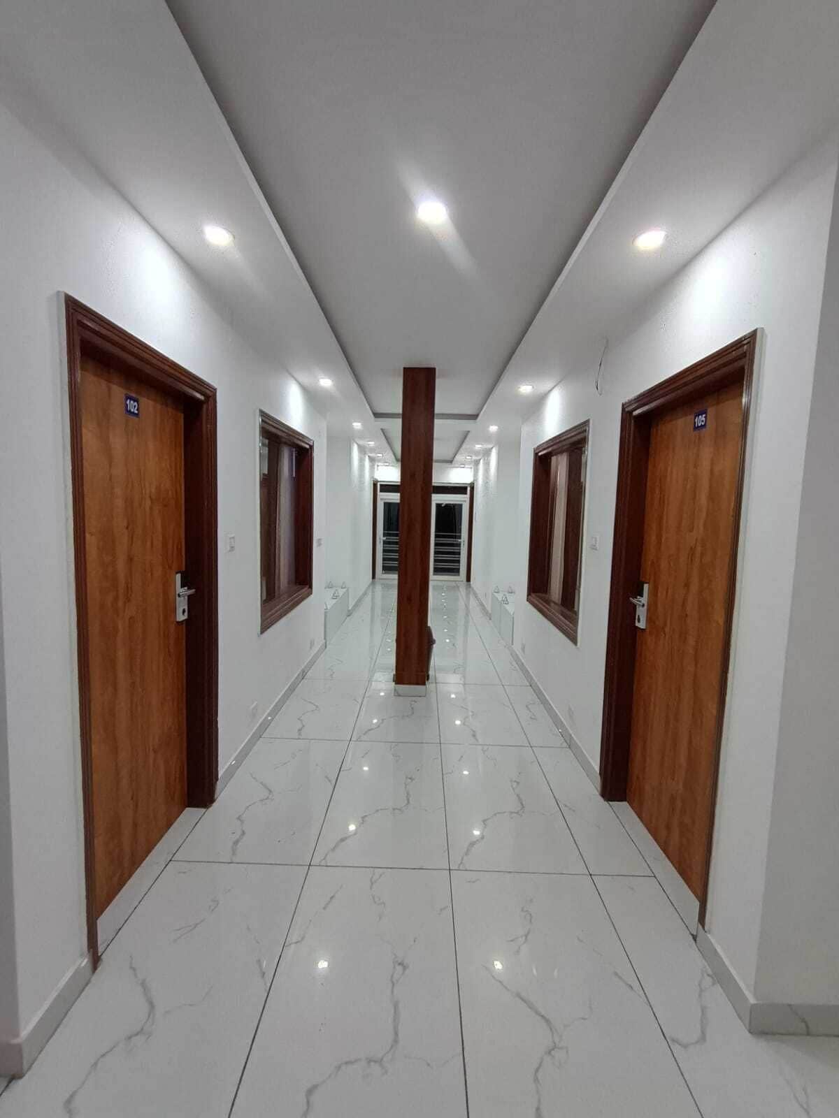 Un pasillo con puertas de madera, números 102 y 105, que conduce a una zona central con una columna.