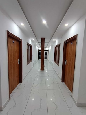 Un pasillo con puertas de madera, números 102 y 105, que conduce a una zona central con una columna.