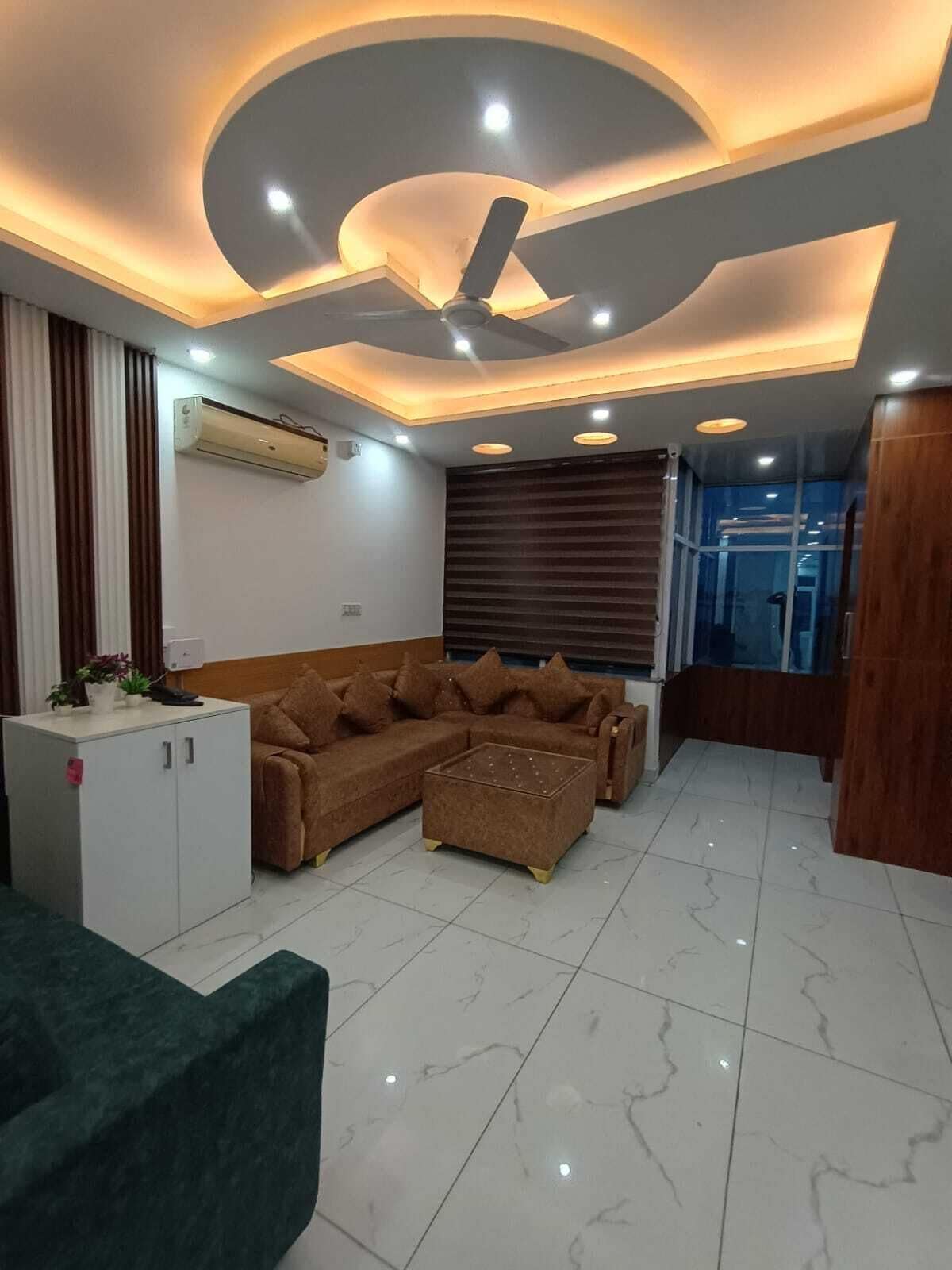 Una sala moderna con sofá seccional, mesa de centro, ventilador de techo, luces empotradas y un ventanal con persianas.