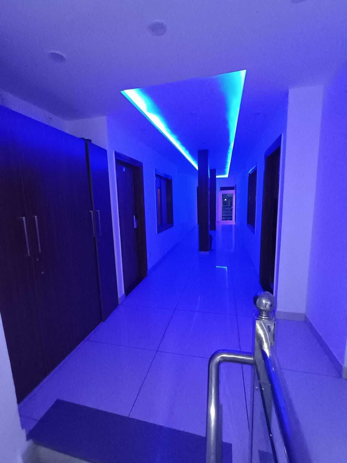 Un couloir au design moderne, avec un chemin rectiligne, des portes de part et d’autre, et un plafond éclairé d’une lumière bleue.