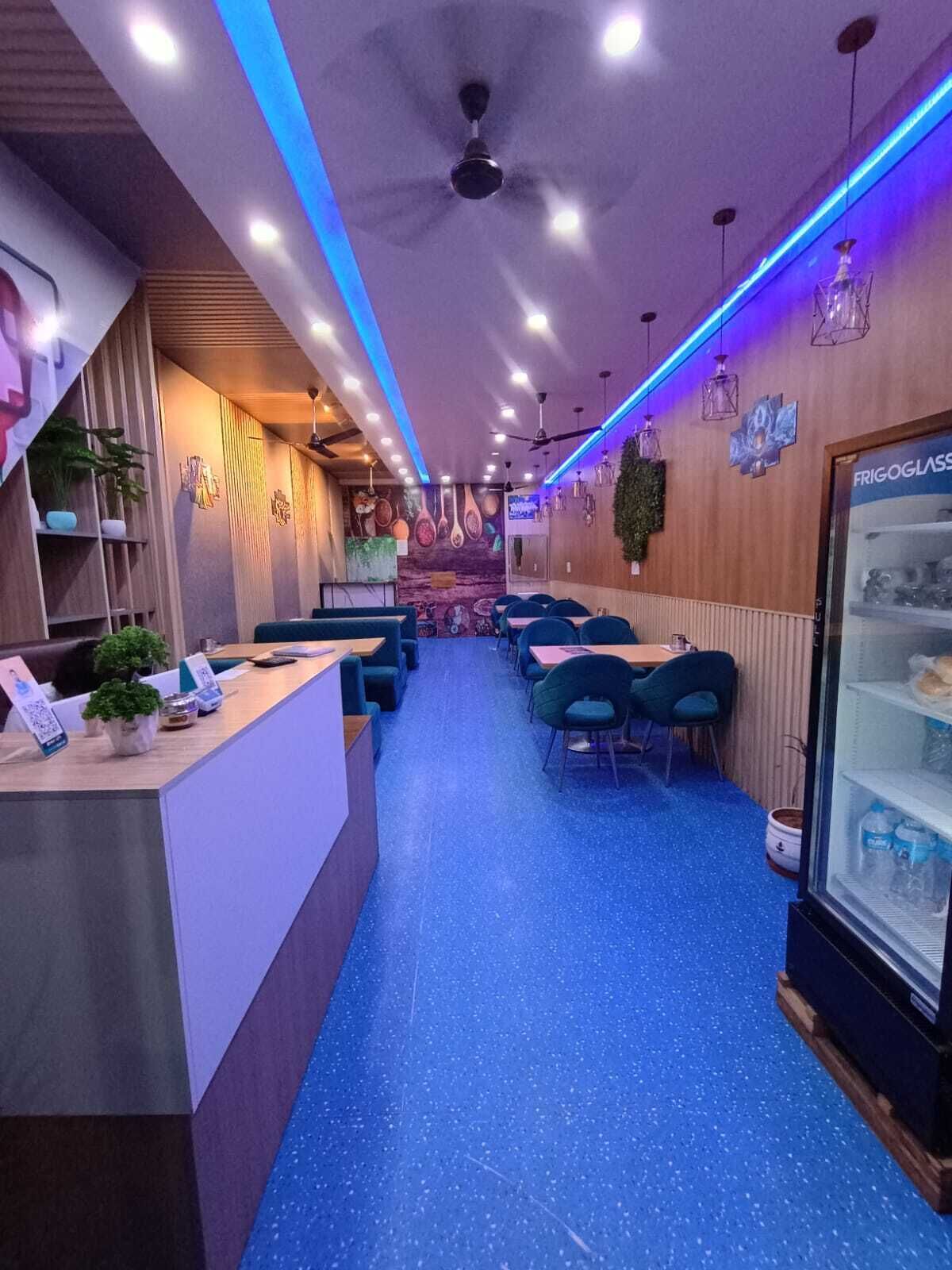 Un interior de restaurante con mostrador, zona de mesas, ventiladores de techo y decoración mural.