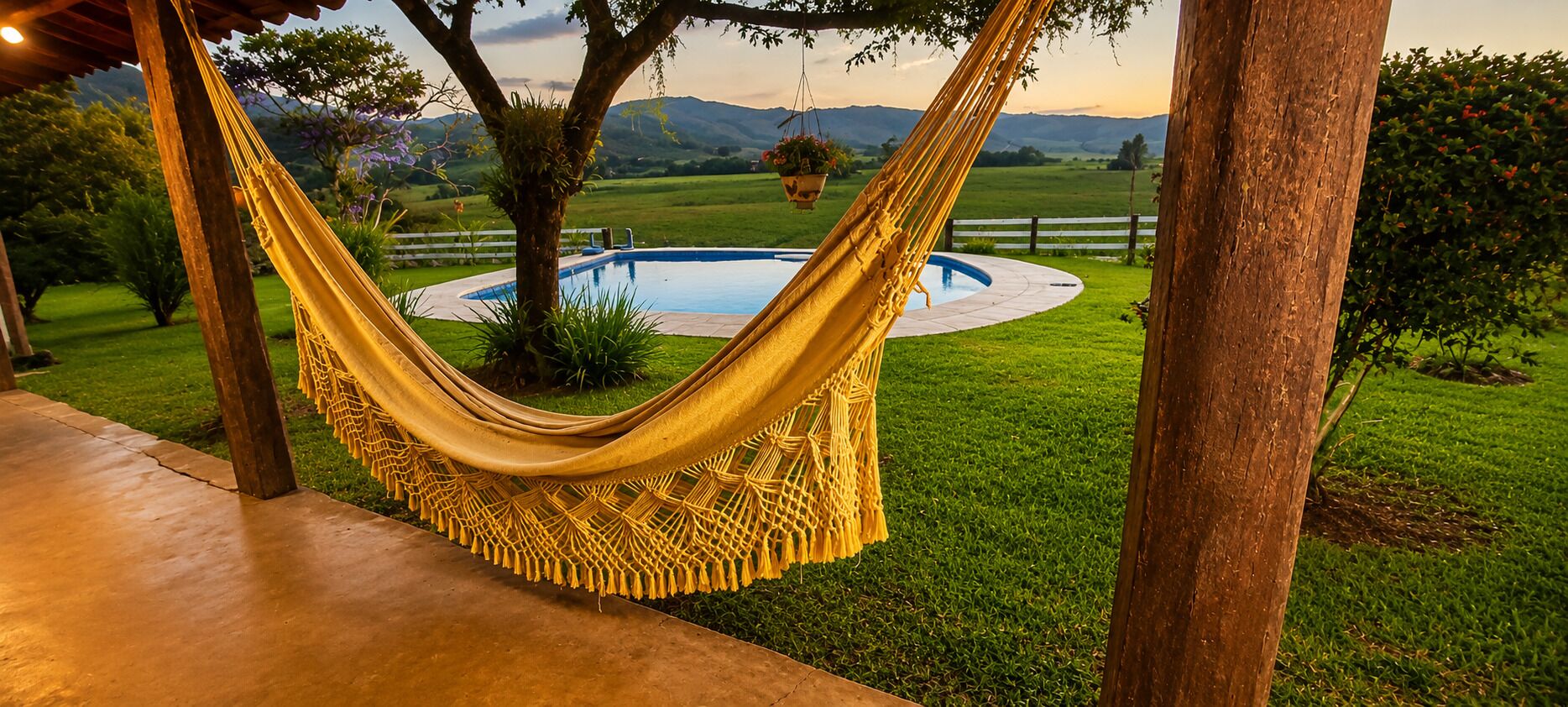 A hammock suspended between trees, a swimming pool, and a grassy landscape with mountains in the background.
