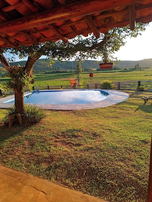A swimming pool under a wooden pergola with a view of a green landscape.