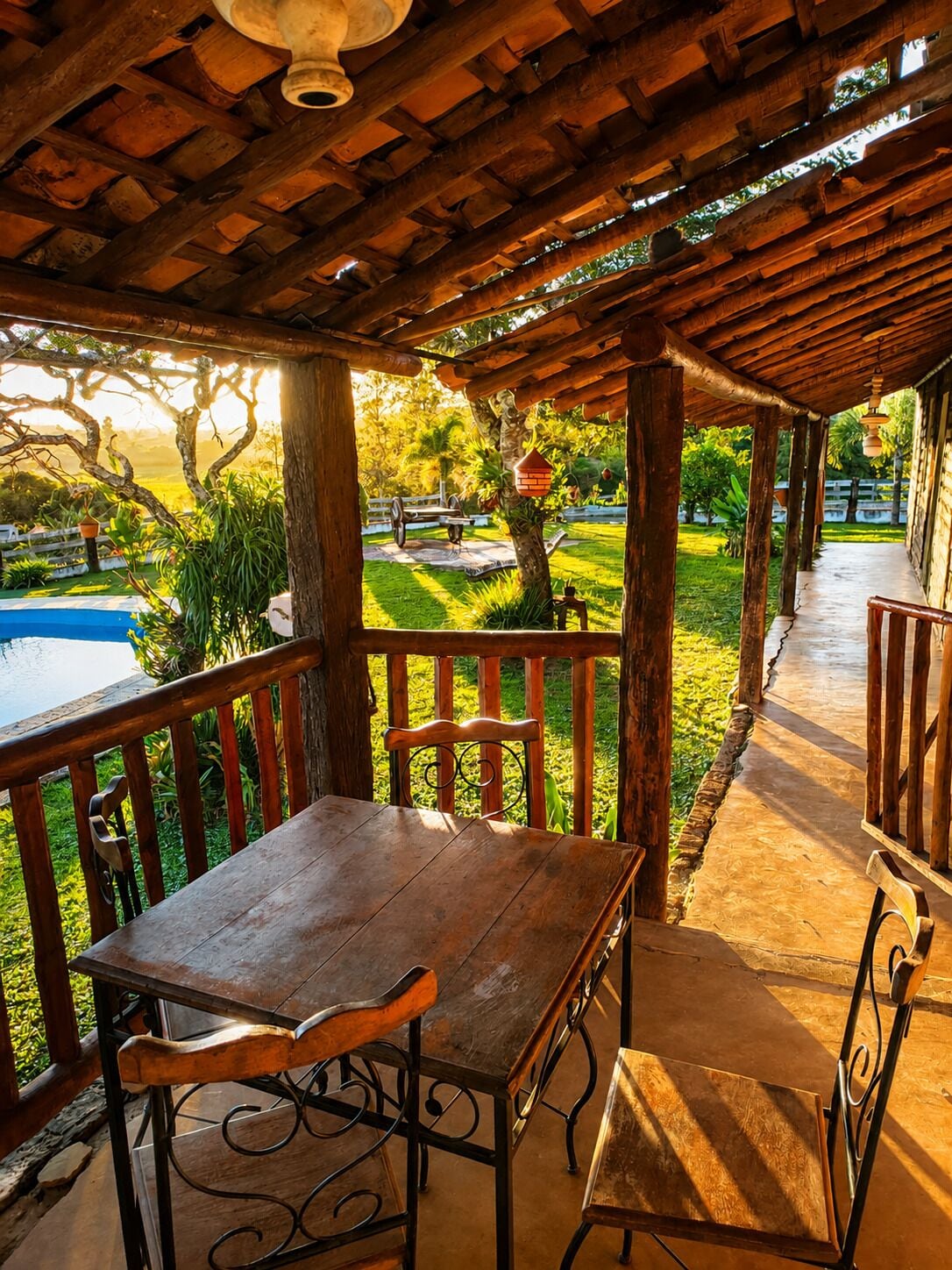 Uma pérgola de madeira com mesa e cadeiras, com vista para uma piscina e um jardim exuberante.