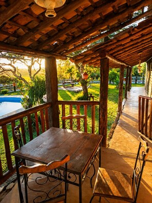 Una pérgola de madera con una mesa y sillas, con vistas a una piscina y un exuberante jardín.