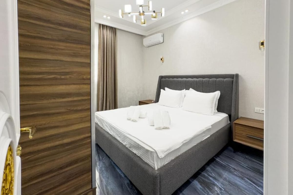 A modern bedroom with a large bed, a wooden door, and a chandelier.
