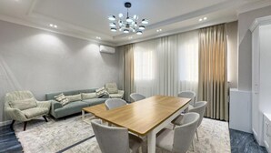Una sala de estar moderna con una mesa de comedor de madera, sillas grises, un sofá gris y un ventanal con cortinas.
