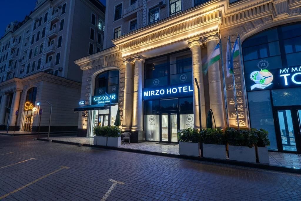 A hotel with a grand entrance, large glass windows, and a sign that reads 'Mirzo Hotel'.