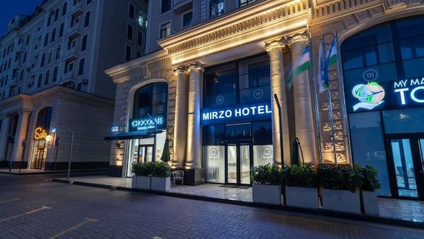 Un hotel con una entrada imponente, amplios ventanales y un letrero que dice 'Mirzo Hotel'.