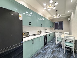 A modern kitchen with a built-in washing machine, a dining area with a table and chairs, and a ceiling light fixture. - Yakkasaray Premium Apartment (Tashkent)