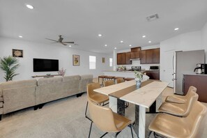 Uma sala de estar moderna com sofá, televisão e área de jantar com mesa e cadeiras.