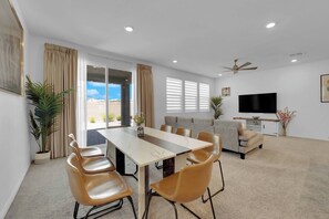 A modern living room with a dining area, a sofa, a TV, and a ceiling fan.