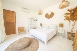 Een slaapkamer met een bed, een stoel, een nachtkastje, een lamp, een mand en een hangende lamp.