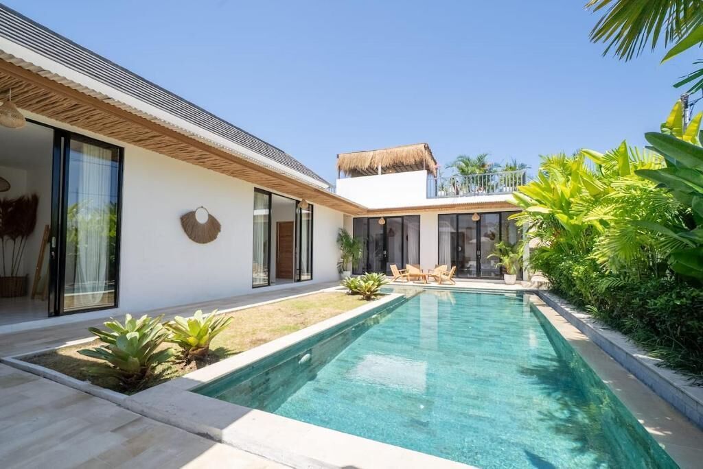 A modern house with a swimming pool, large windows, and a thatched roof.