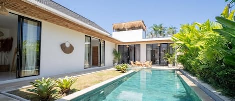Una casa moderna con piscina, ventanas amplias y techo de paja.
