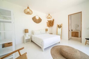 Ein Schlafzimmer mit einem Bett, Nachttischen, einem Sessel, einem Spiegel und einer Tür.