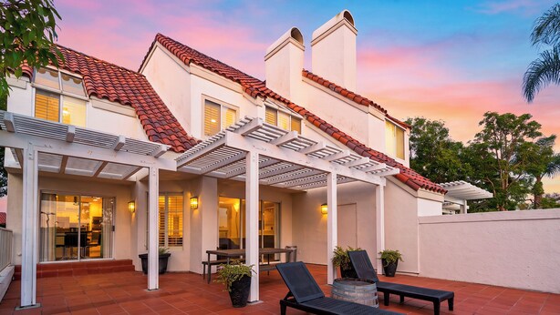 Ein Haus mit überdachter Terrasse, Gartenmöbeln und Blick auf den Sonnenuntergang.