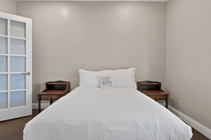 Ein Schlafzimmer mit einem großen Bett, zwei Nachttischen, einem Beistelltisch und einer Tür mit Milchglasverkleidungen.