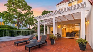 Eine überdachte Terrasse mit zwei Liegestühlen, einem Tisch und Topfpflanzen.