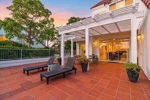 A covered patio with two lounge chairs, a table, and potted plants. - Pergola Terrace + Fireplace + Pool + Gym | Salt Creek + Harbor | Terracotta (Dana Point)
