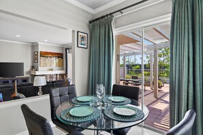 A modern living room with a glass dining table, black leather chairs, a flat-screen TV, and artwork on the walls. - Pergola Terrace + Fireplace + Pool + Gym | Salt Creek + Harbor | Terracotta (Dana Point)