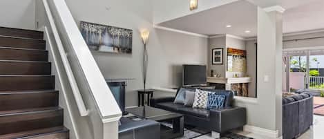 Ein modernes Wohnzimmer mit Treppe, Flachbildfernseher und Couchtisch.