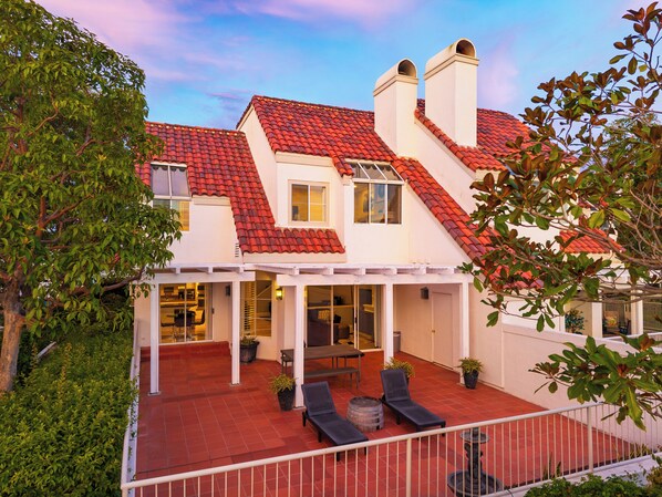 Ein zweistöckiges Haus mit rotem Ziegeldach, einer Veranda mit Gartenmöbeln und einem Garten.
