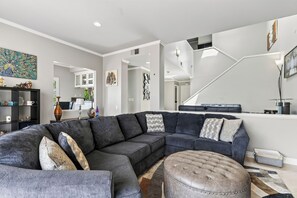 Ein modernes Wohnzimmer mit einem Ecksofa, einem Hocker und einer Treppe, die in eine weitere Ebene führt.