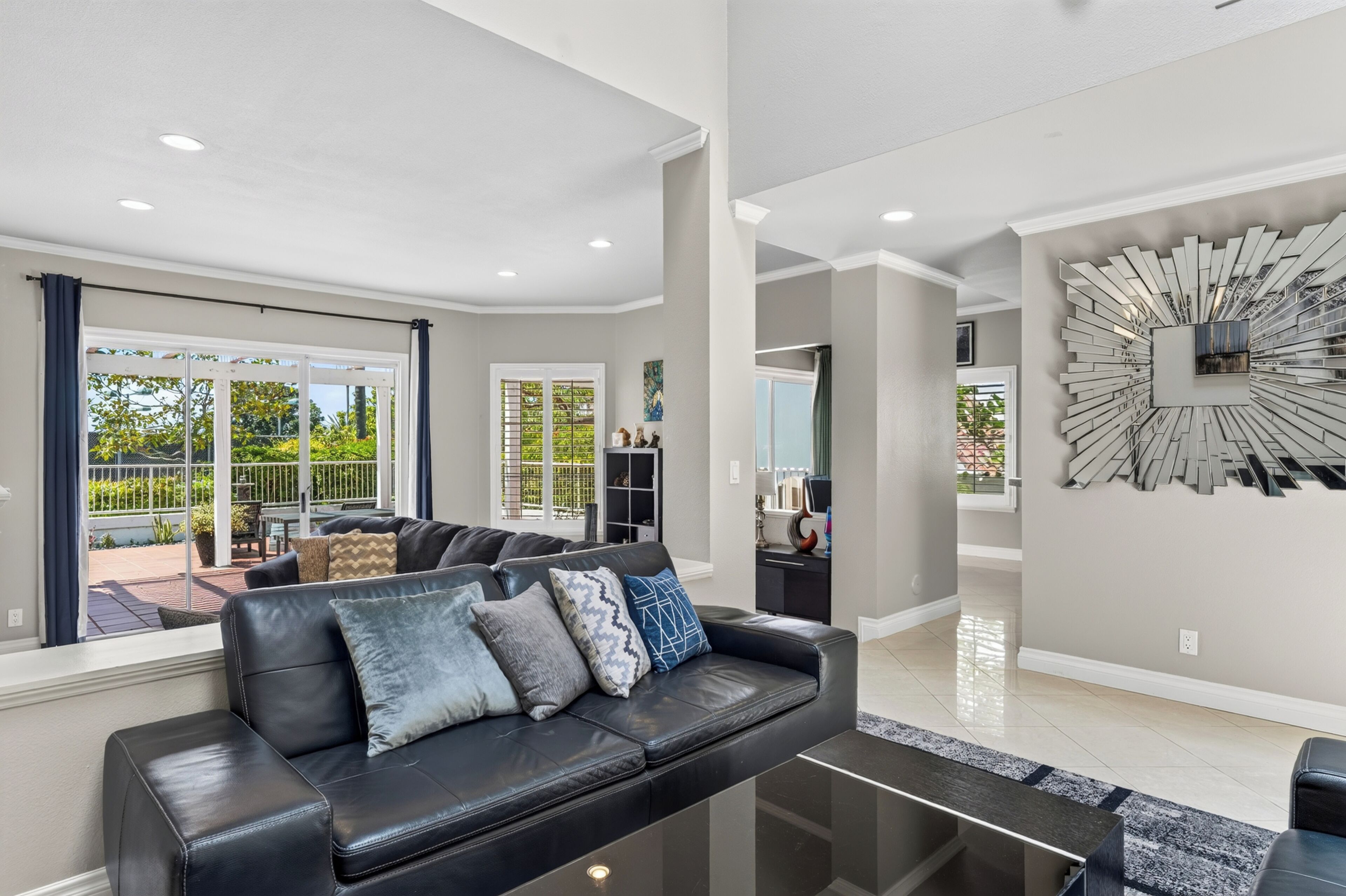 A modern living room with a black leather sofa, a glass coffee table, and a large abstract wall art piece.