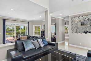 A modern living room with a black leather sofa, a glass coffee table, and a large abstract wall art piece. - Pergola Terrace + Fireplace + Pool + Gym | Salt Creek + Harbor | Terracotta (Dana Point)