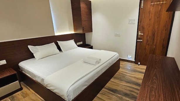 Una habitación de hotel con una cama grande, cabecera de madera, una mesita de noche y piso de madera.