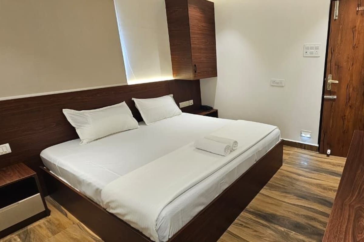Una habitación de hotel con una cama grande, cabecera de madera, una mesita de noche y piso de madera.