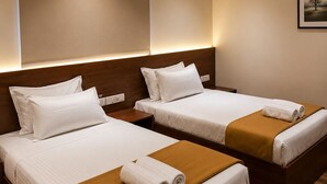 Habitación de hotel con dos camas, cada una con sábanas blancas y mantas marrones, un ventilador de techo y un equipo de aire acondicionado.