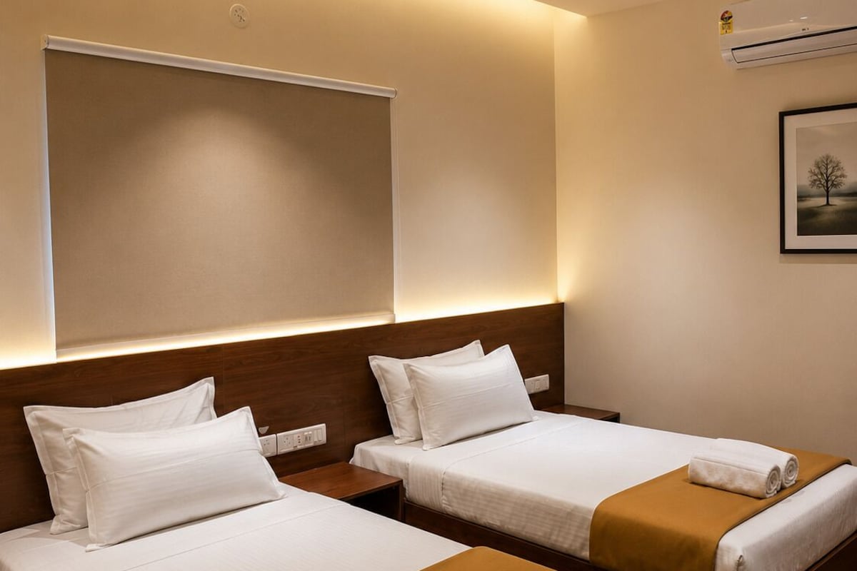 Habitación de hotel con dos camas, cada una con sábanas blancas y mantas marrones, un ventilador de techo y un equipo de aire acondicionado.