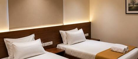 A hotel room with two beds, each with white linens and brown throw blankets, a ceiling fan, and an air conditioning unit.