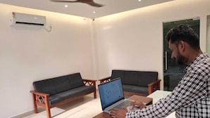 Una habitación con una computadora portátil sobre una mesa de madera, dos sofás y un equipo de aire acondicionado en la pared.