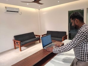 Una habitación con una computadora portátil sobre una mesa de madera, dos sofás y un equipo de aire acondicionado en la pared.
