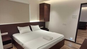 Una habitación de hotel moderna con una cama grande, cabecera de madera, ventilador de techo y piso de madera.