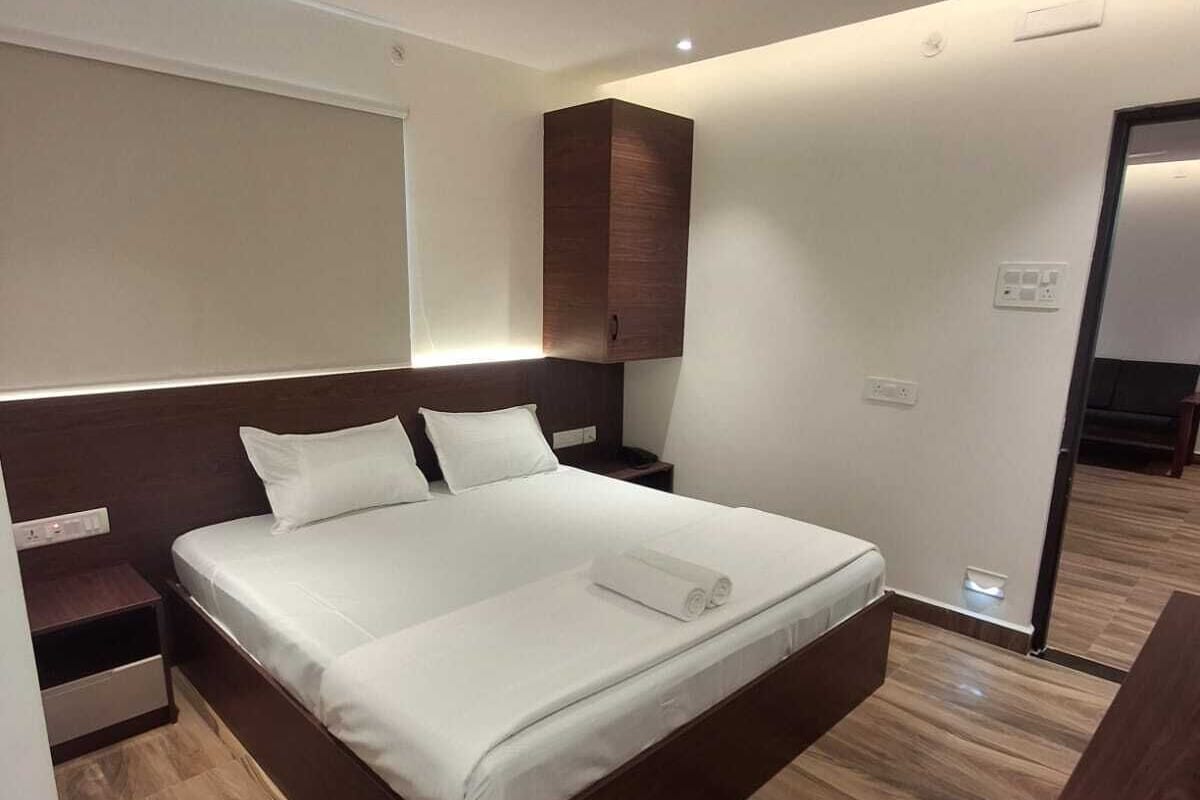 Una habitación de hotel moderna con una cama grande, cabecera de madera, ventilador de techo y piso de madera.