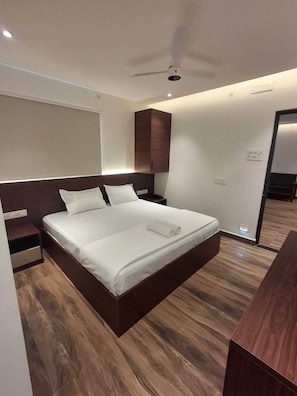 A modern hotel room with a large bed, a wooden headboard, a ceiling fan, and a wooden floor.