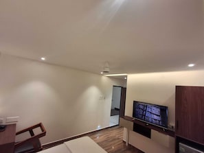A modern living room with a flat-screen TV, wooden furniture, and recessed ceiling lighting.