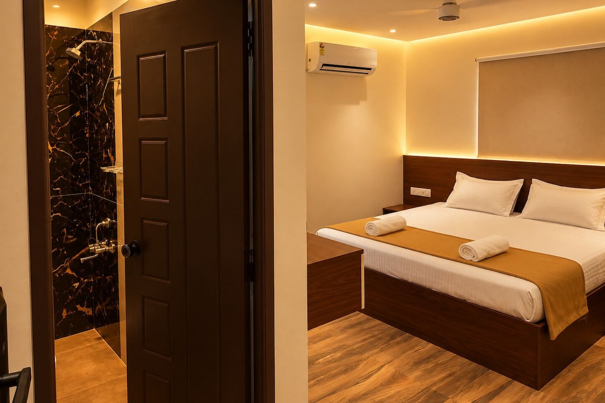 Habitación de hotel con cama, mesita de noche, equipo de aire acondicionado y zona de ducha con paredes de mármol.