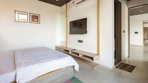 A bedroom with a bed, a TV mounted on the wall, and a door leading to another room.