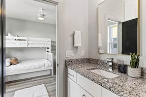 A modern bedroom with bunk beds, a ceiling fan, a bathroom with a granite countertop, sink, and mirror. - Open-Concept Design + Game Stash | Mins to Five Points | Harmony House (Nashville)