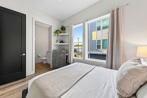 A bedroom with a bed, a dresser, a window with curtains, and a view of the outside. - Open-Concept Design + Game Stash | Mins to Five Points | Harmony House (Nashville)