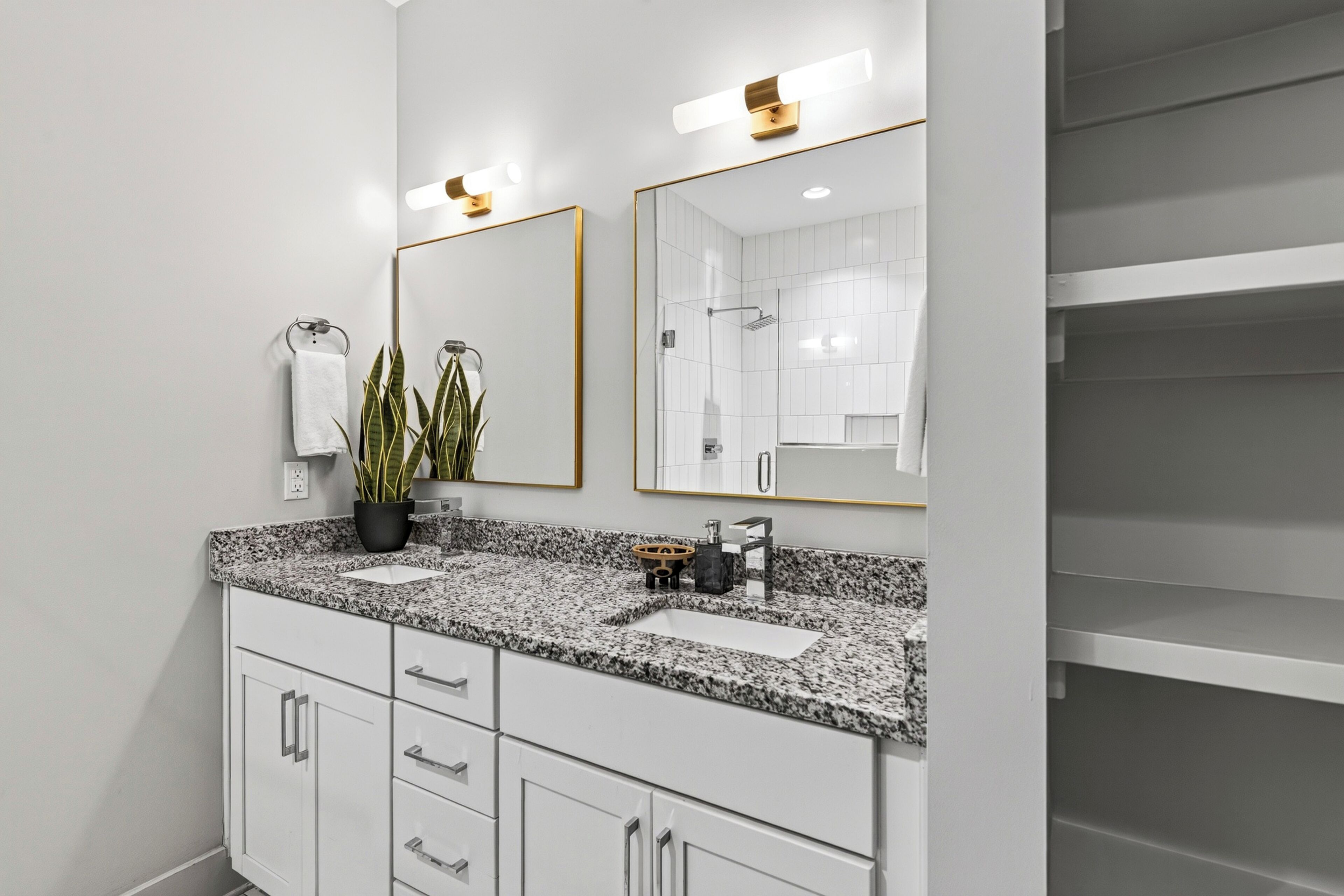 A modern bathroom with a granite countertop, two sinks, a large mirror, and a shower area.