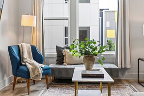 A modern living room with a blue armchair, a grey sofa, a coffee table, and a potted plant. - Open-Concept Design + Game Stash | Mins to Five Points | Harmony House (Nashville)