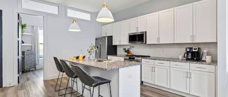 Una cocina moderna con armarios blancos, encimera de granito y una isla central con taburetes de bar.
