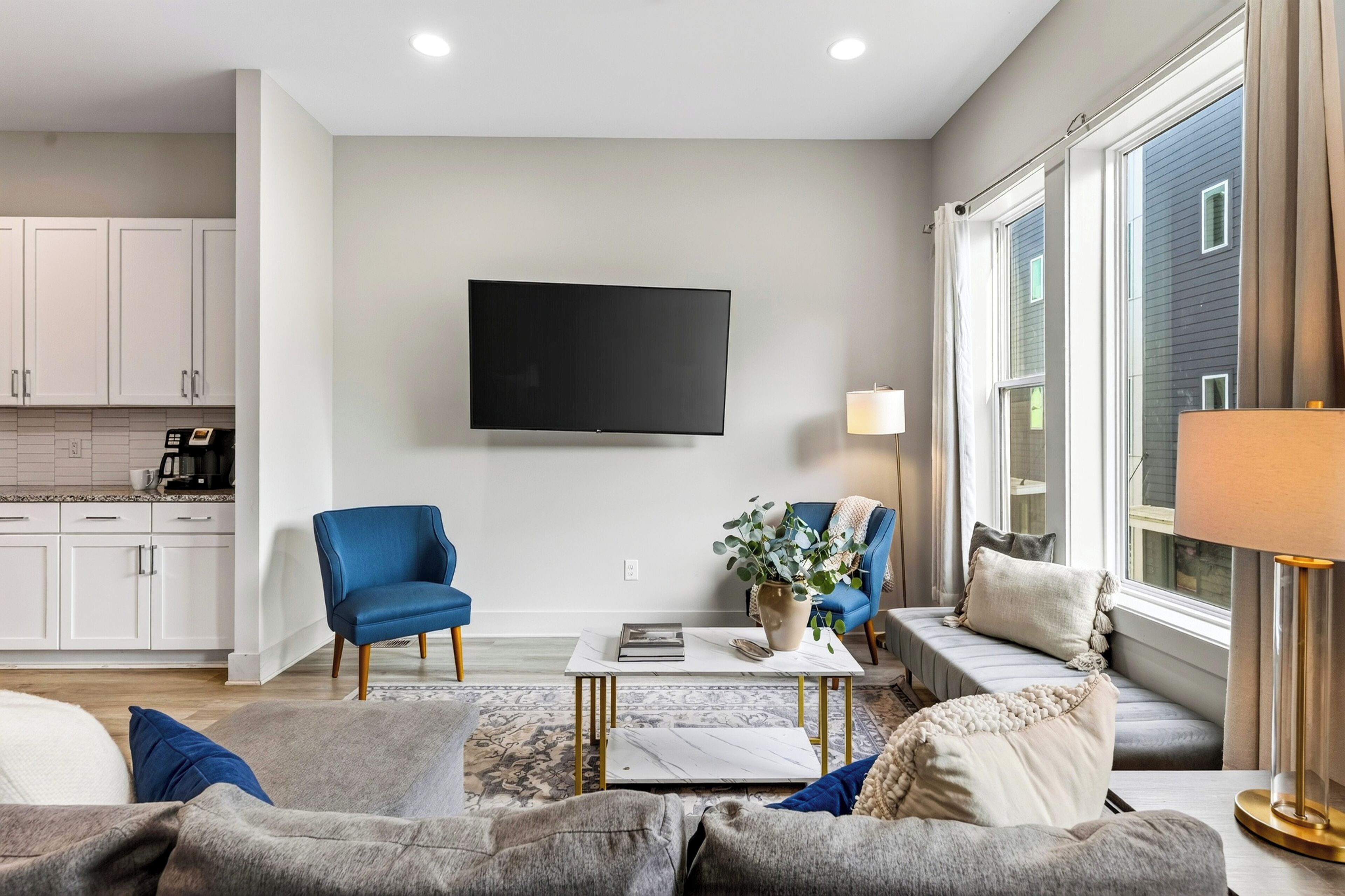 A modern living room with a flat-screen TV, two blue armchairs, a sofa, and a coffee table.