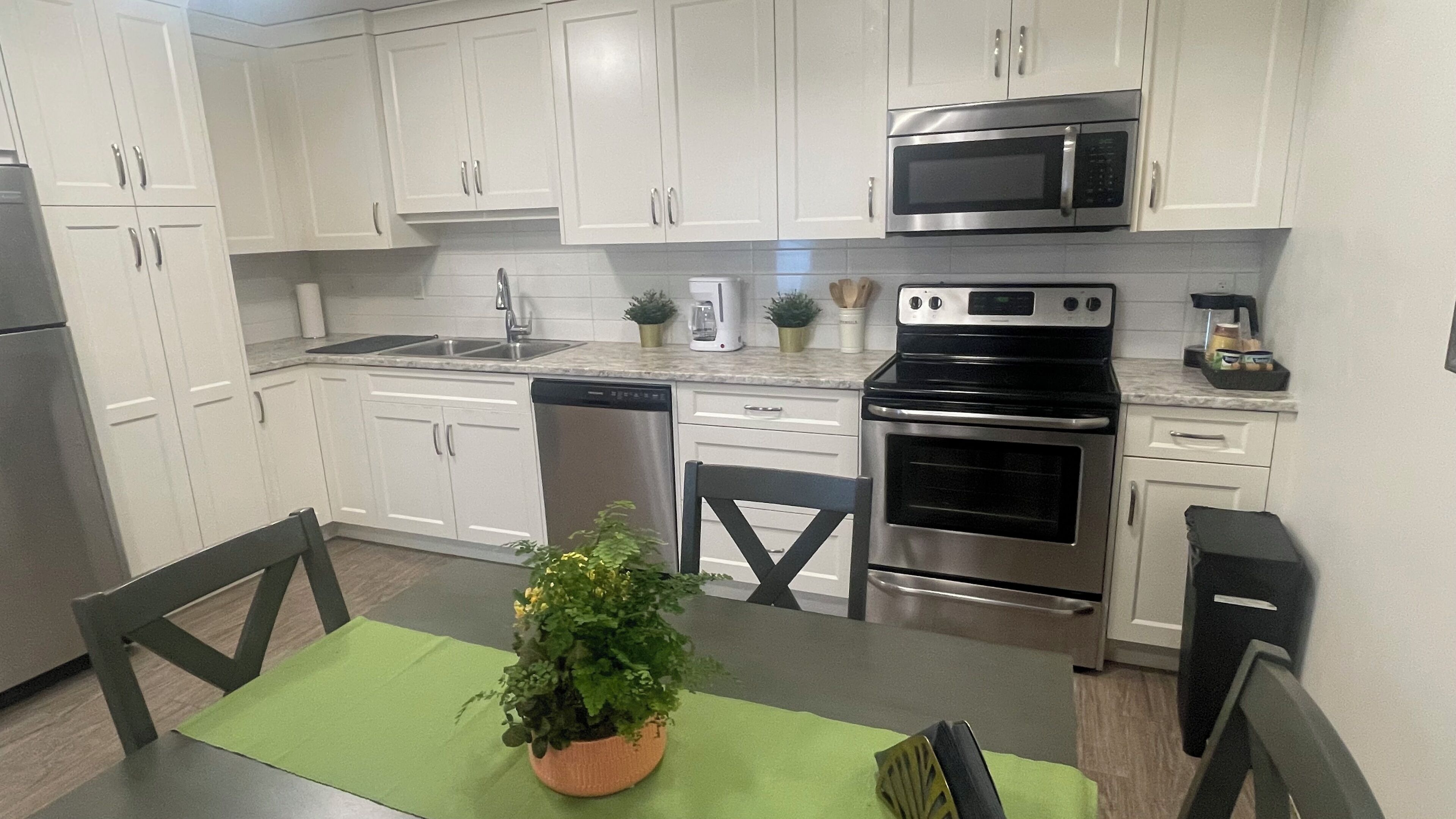 A modern kitchen with white cabinets, stainless steel appliances, and a green table with a potted plant.